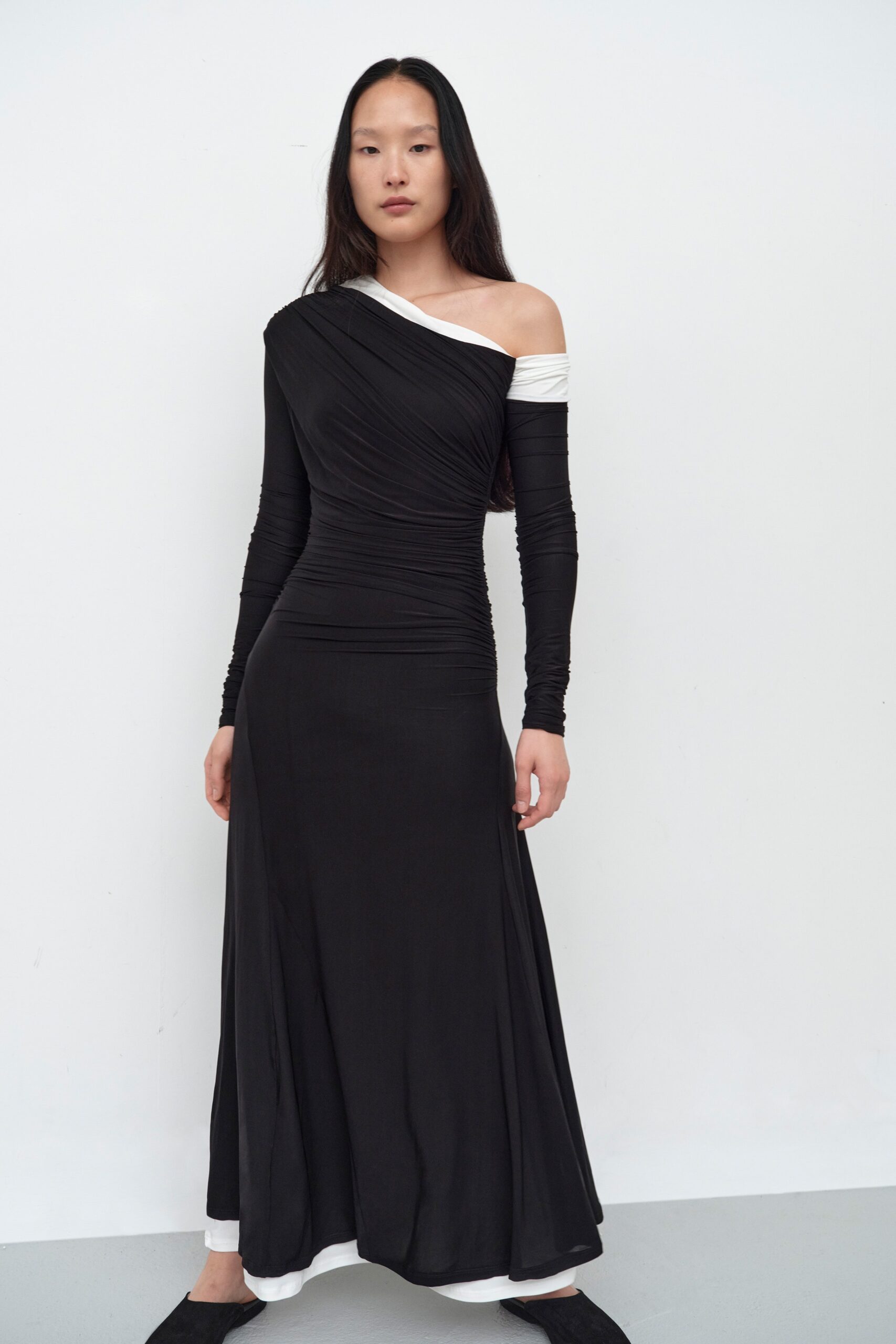 A fitted black dress with long sleeves and an off-shoulder design featuring draped detailing.