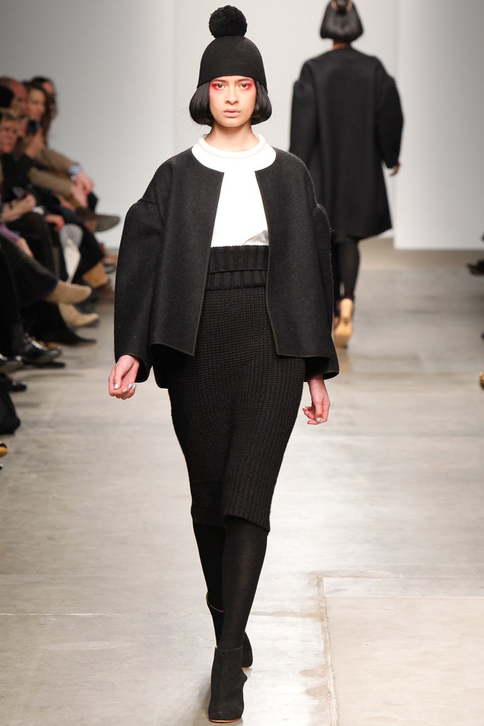 A fitted black wool top with long sleeves paired with a black skirt, featuring an asymmetric design.