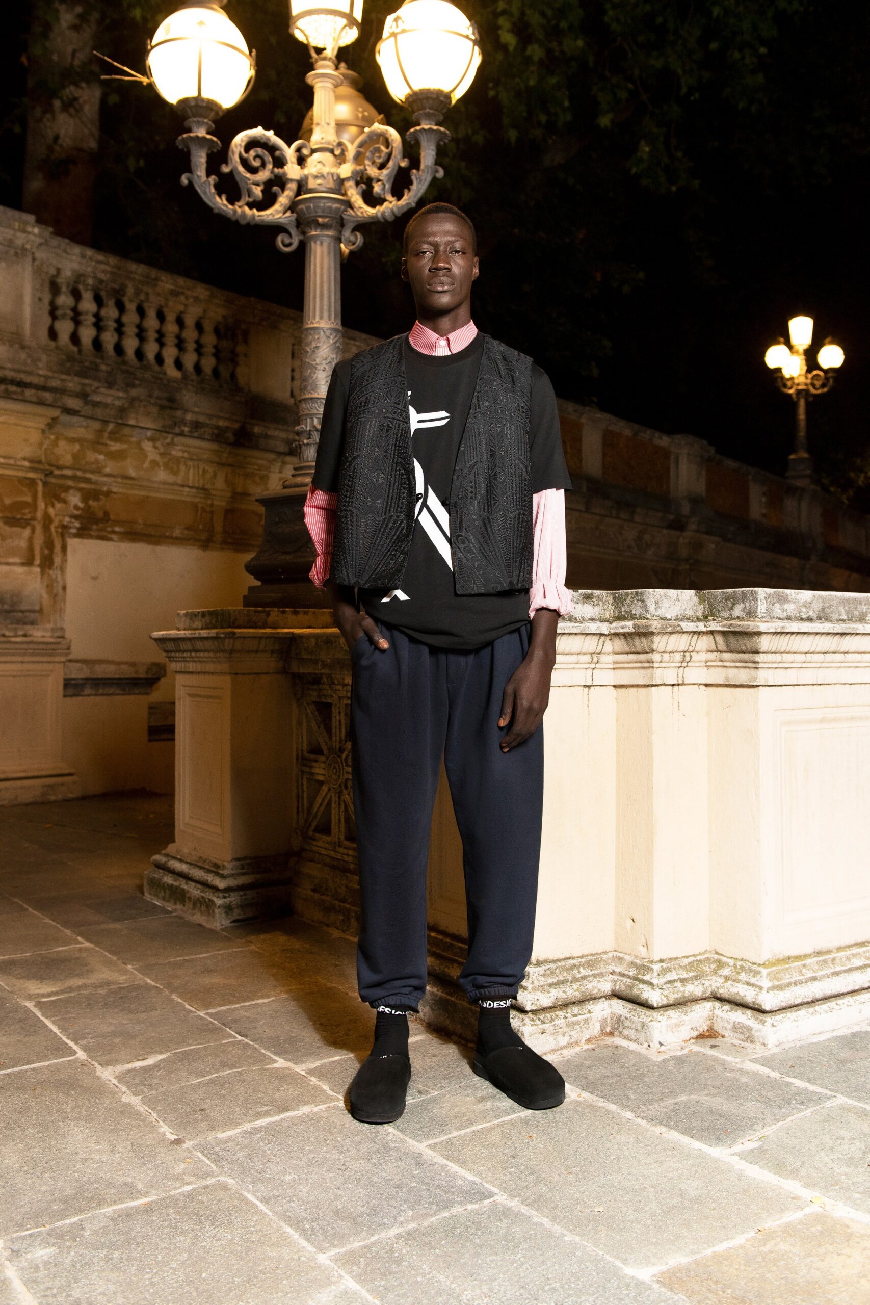 A relaxed black vest over a long-sleeve pink shirt paired with navy pants.