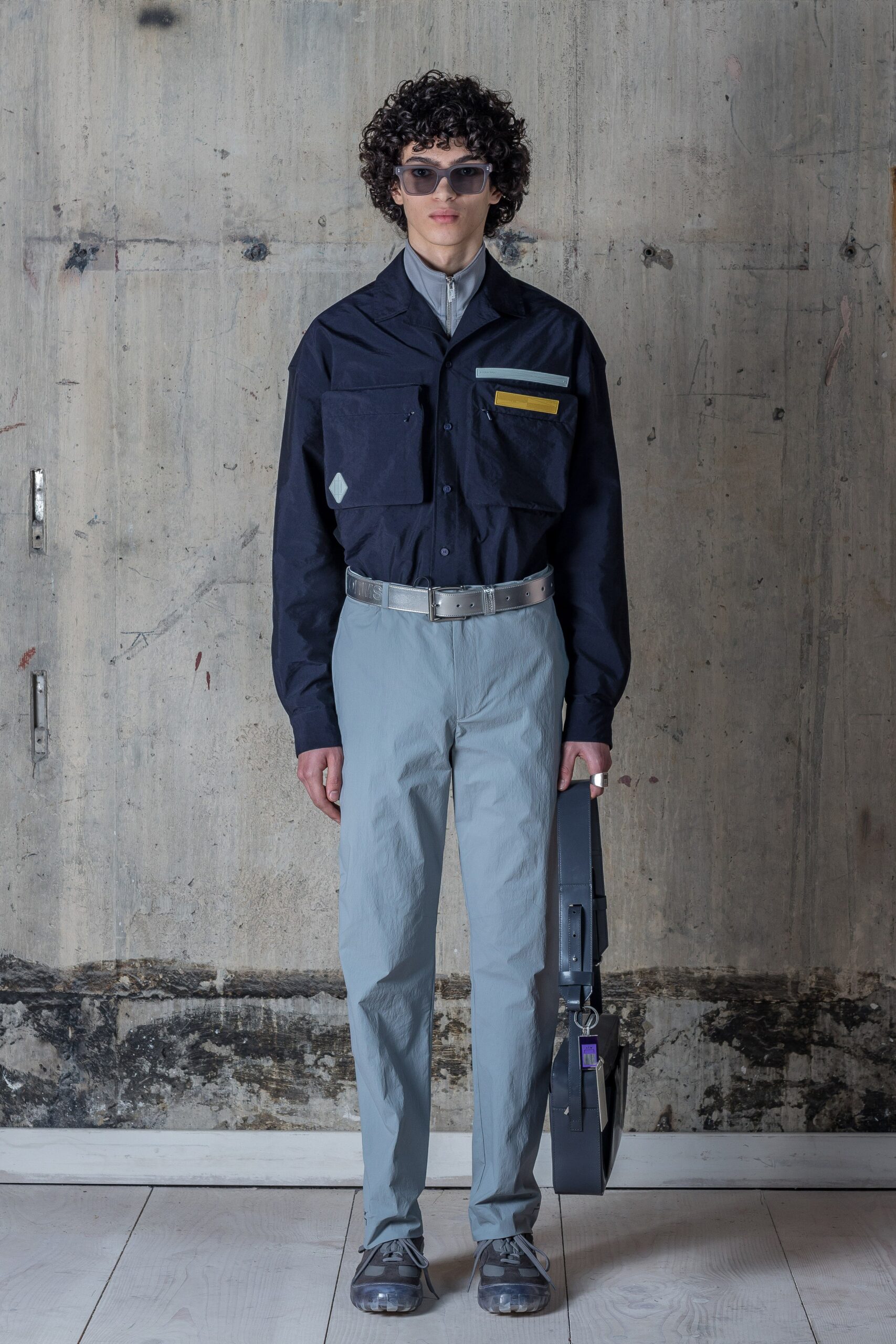 A relaxed long-sleeve shirt in black, featuring a classic collar and buttoned front, paired with light gray pants that enhance the overall silhouette. The addition of a pocket detail adds a functional yet stylish touch, creating a contemporary look that balances structure and ease.