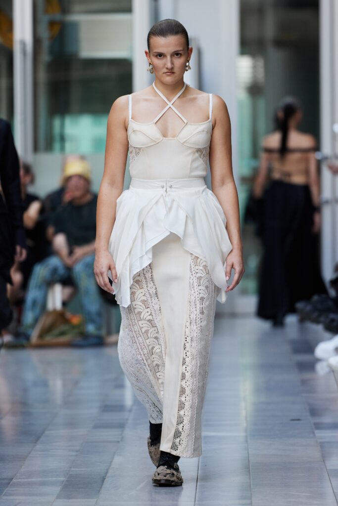 An asymmetric white cotton sleeveless dress featuring intricate lace detailing and a flowing silhouette.