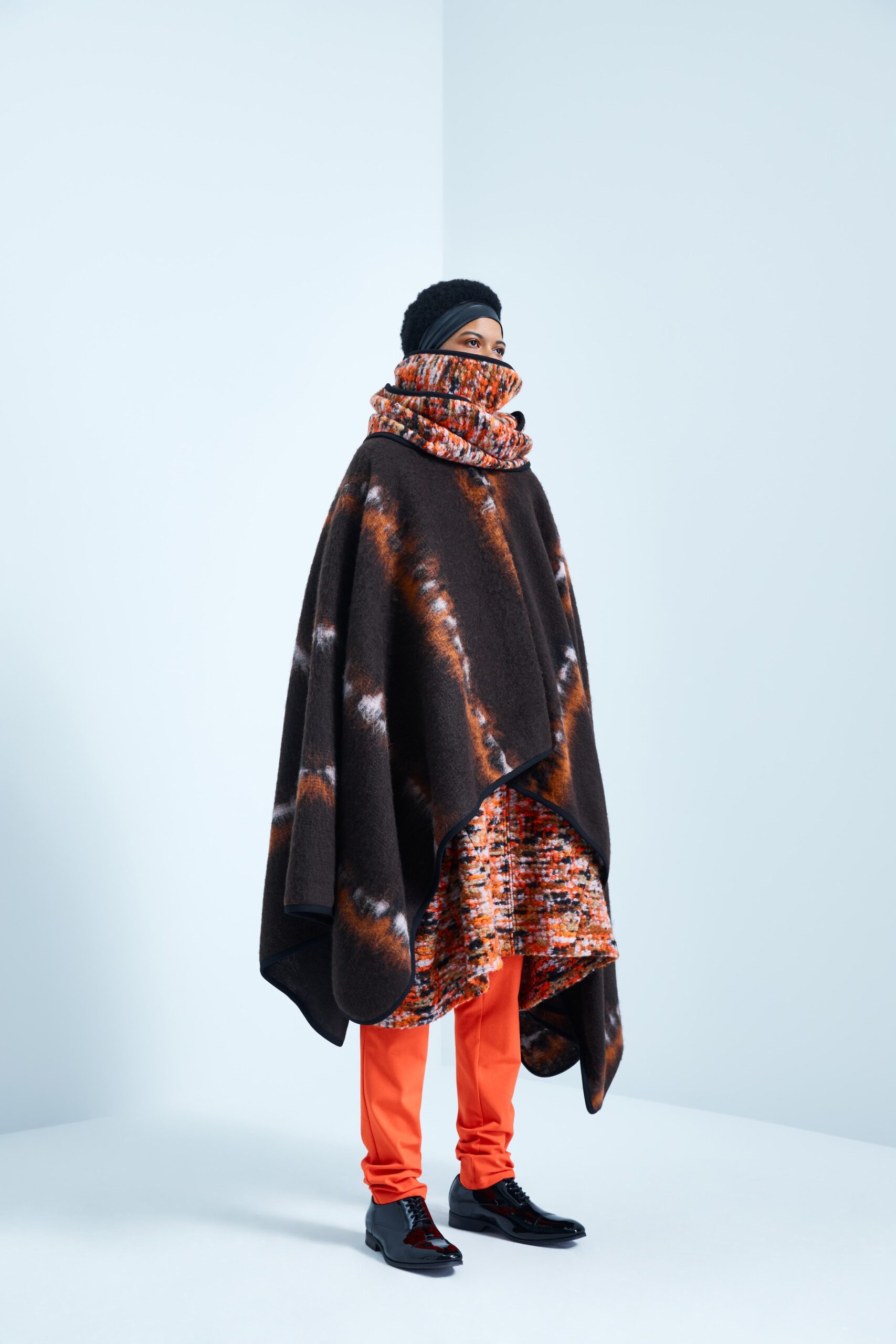 This ensemble features a relaxed poncho crafted from rich brown wool, layered over a vibrant printed dress. The high-neck design adds an intriguing element, while the interplay of colors and textures creates a dynamic visual experience.