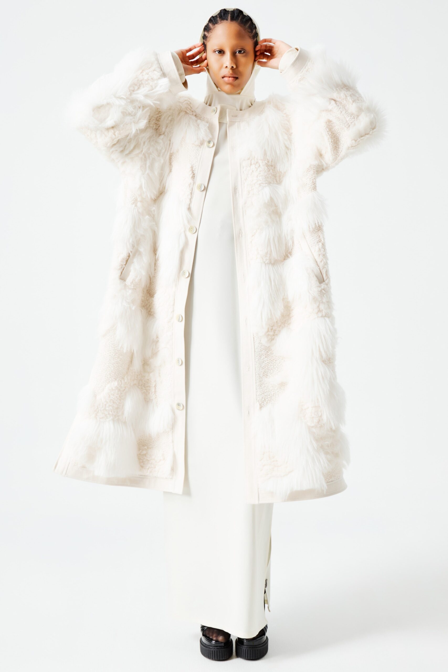 This ensemble features a striking white fur coat layered over a fitted dress, creating a bold contrast in textures. The high-neck design and long sleeves of the coat add a sense of sophistication, while the asymmetric detailing introduces a modern edge to the overall silhouette.