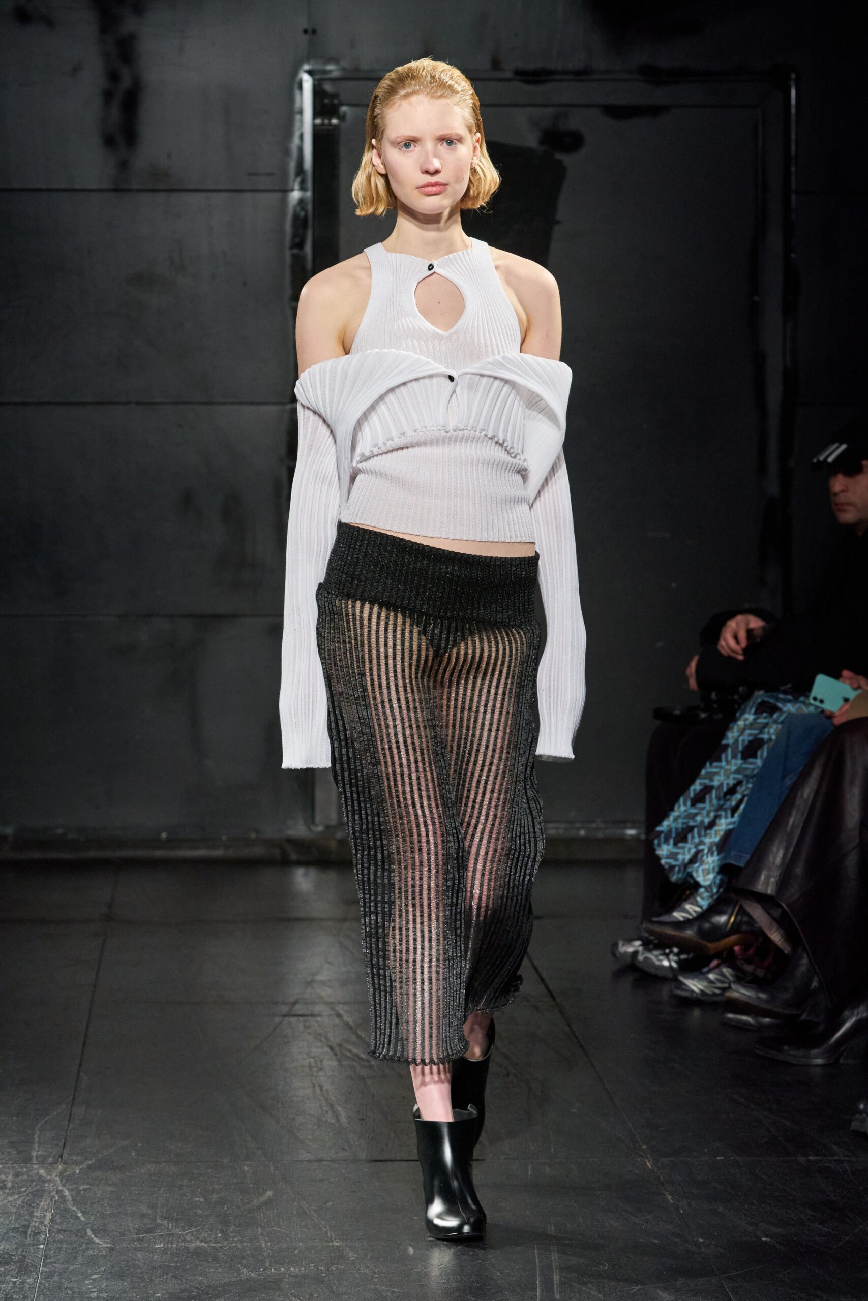 A fitted white off-shoulder top with long sleeves paired with a sheer black skirt.