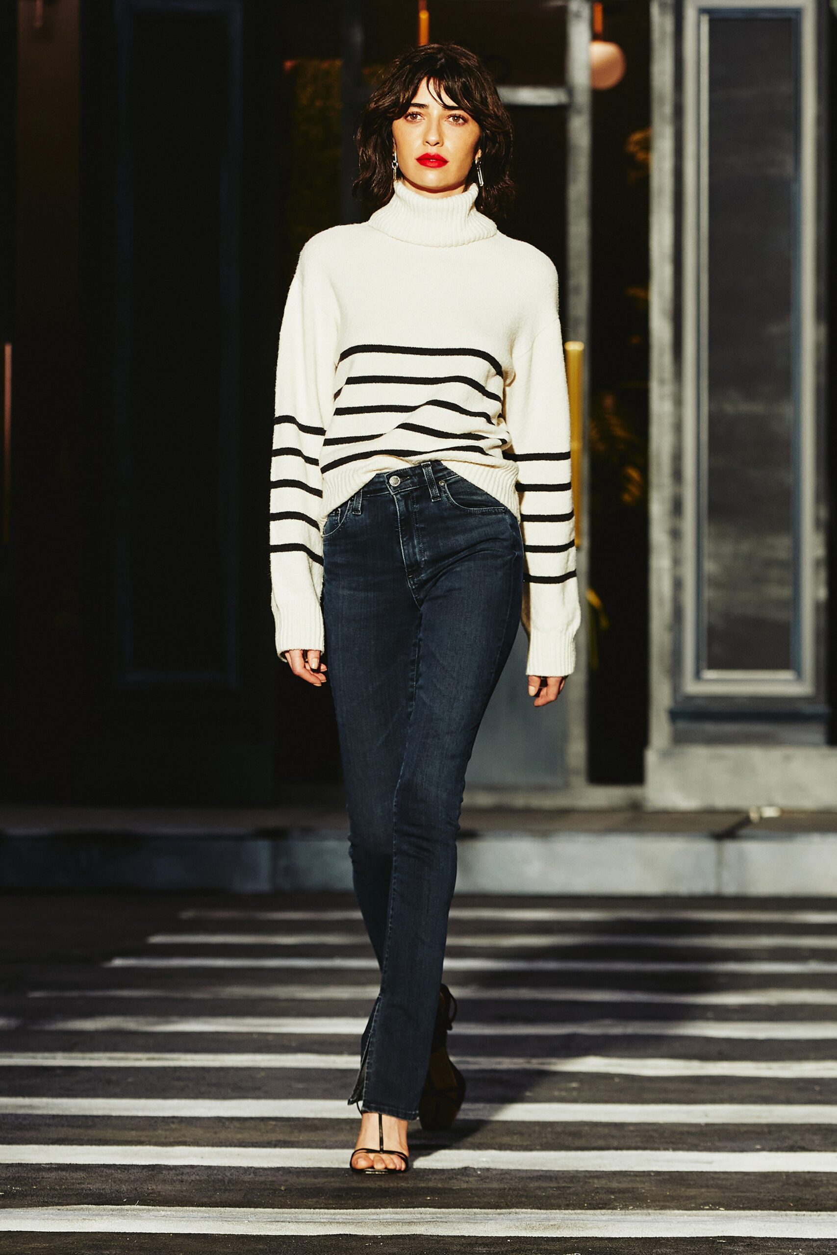 A fitted striped white and black sweater with long sleeves and a turtleneck, paired with fitted jeans.