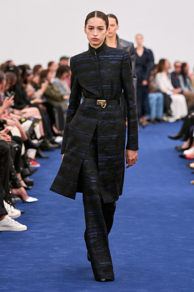 A fitted black and blue wool coat with long sleeves and an asymmetric design, paired with tailored pants.