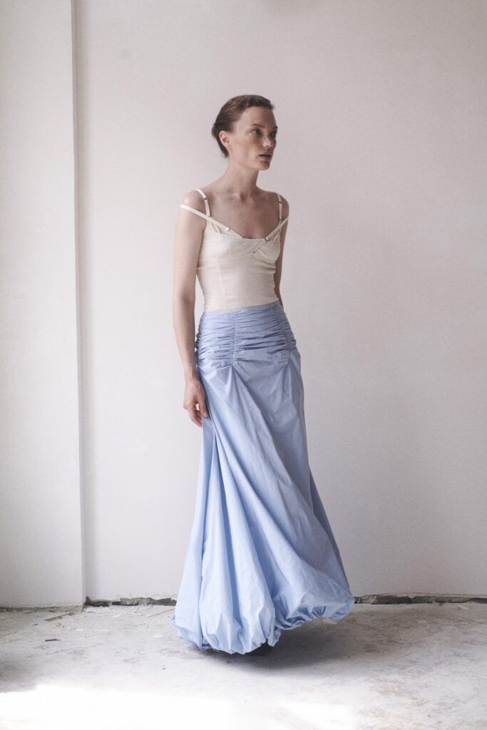 A fitted blue dress with pleated details, sleeveless design, and a V-neckline.