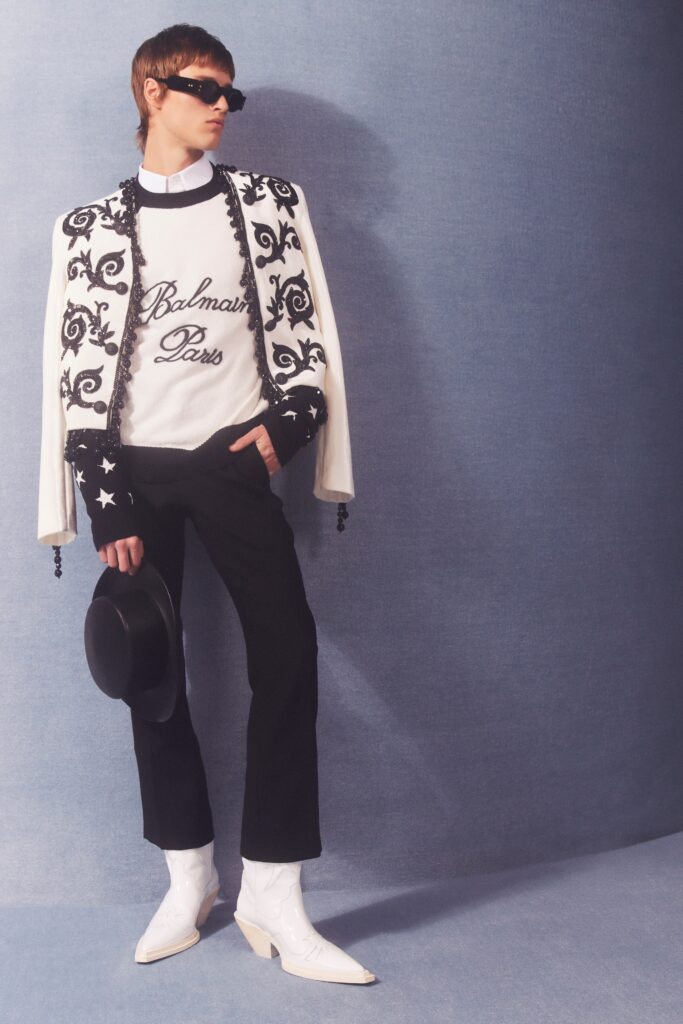 A tailored black and white jacket with intricate designs paired with black pants.