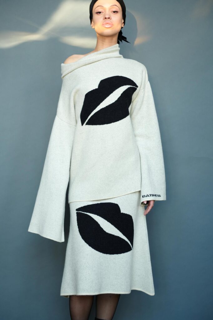 A relaxed beige wool off-shoulder dress featuring a bold lip print.
