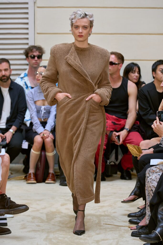 A relaxed brown faux-fur coat with long sleeves and a collared design, featuring a belted detail.