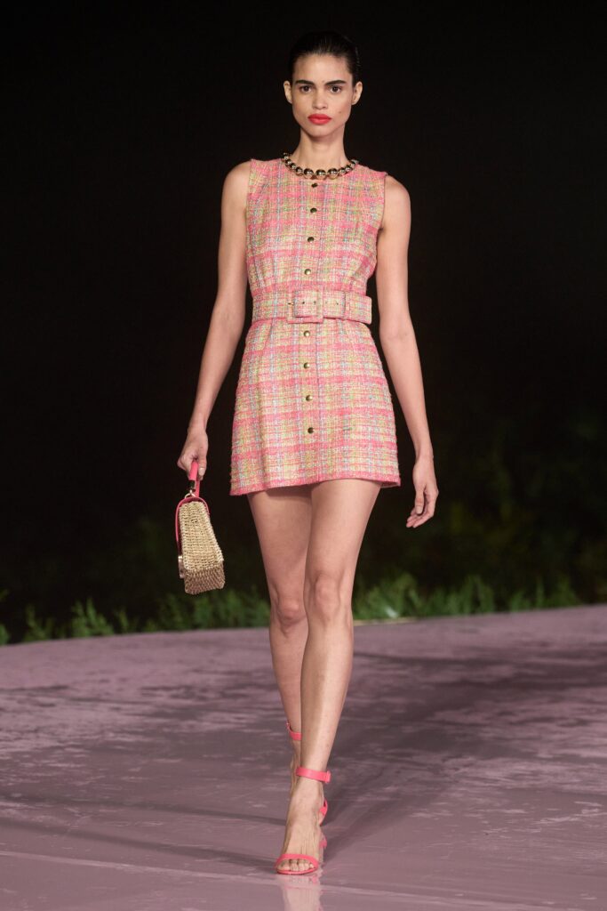 A fitted pink tweed dress with a sleeveless design, collared neckline, and buttoned details.