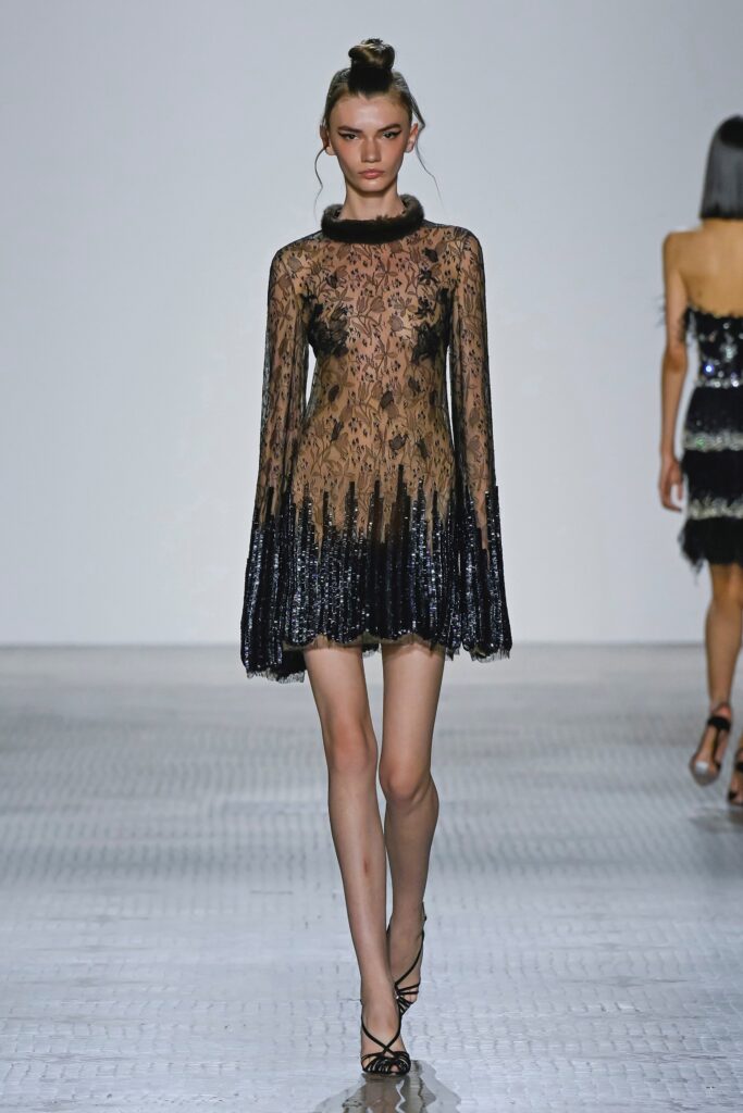 A fitted black lace dress with long sleeves, a high neckline, and tiered design details.