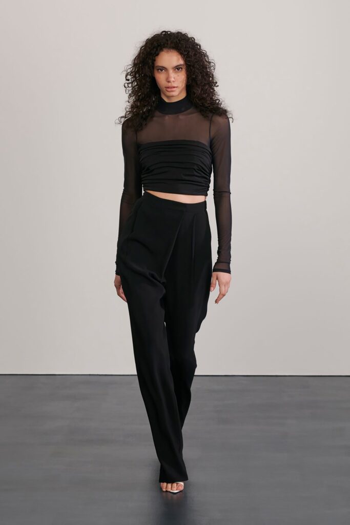 A fitted black silk long-sleeve top with pleated details paired with wide-leg pants.