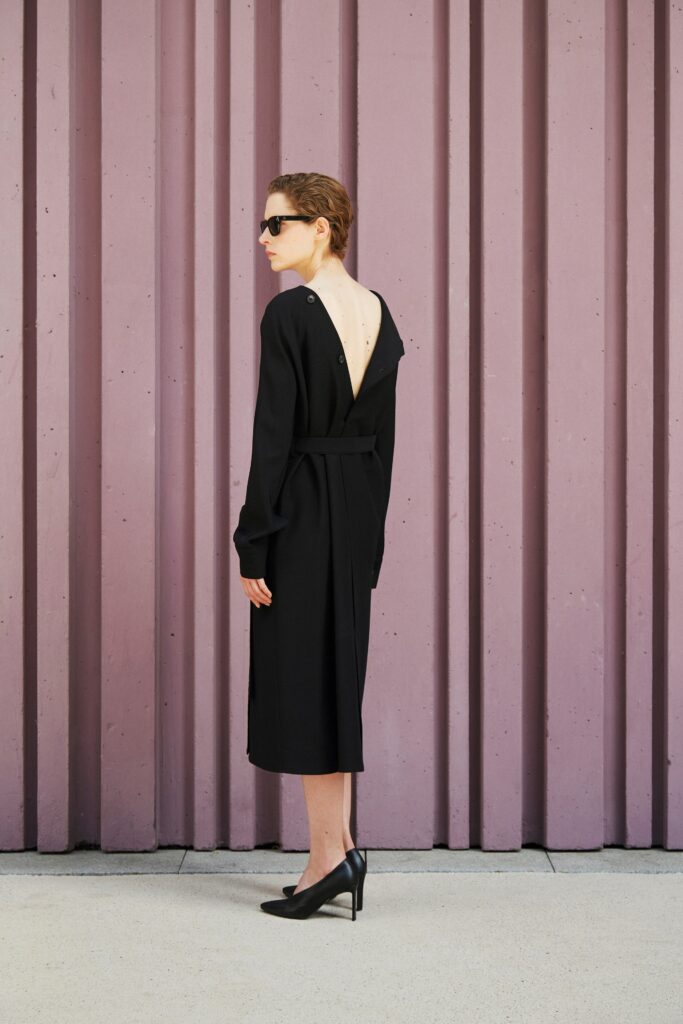 A relaxed black dress with long sleeves and a V-neckline featuring an asymmetric design.