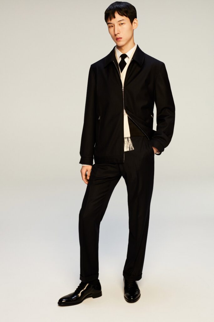 A fitted black cotton jacket with long sleeves and collared design, paired with straight-leg pants.