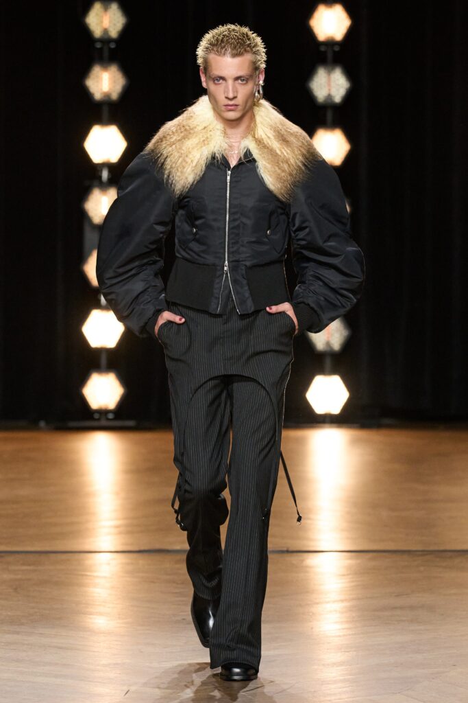 A fitted black leather jacket with a collared neckline paired with striped pants.