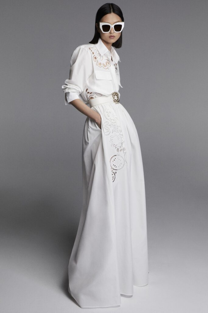 A fitted white dress with long sleeves, a collared neckline, and embroidered A-line details.
