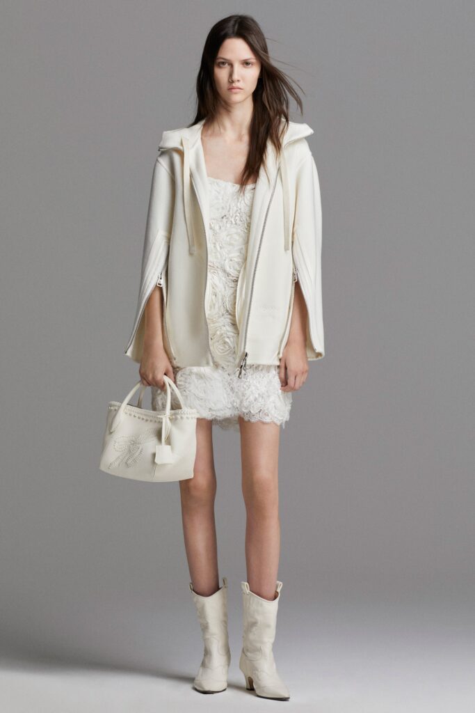 A fitted white sleeveless dress layered with a hooded coat for a chic look.