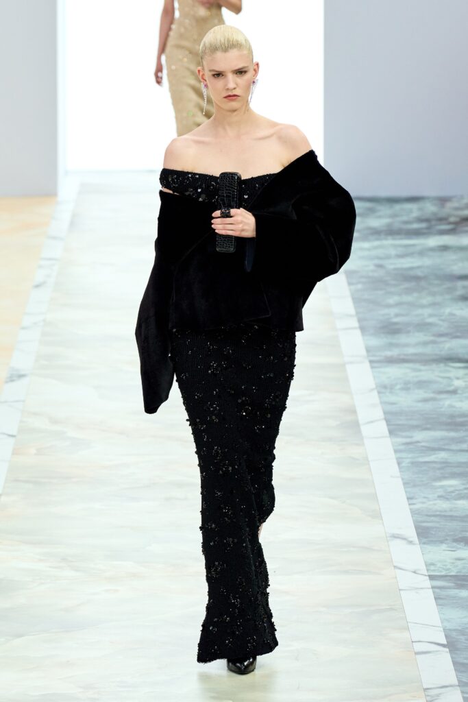 A fitted black velvet off-shoulder dress adorned with sequins and a straight-leg silhouette.