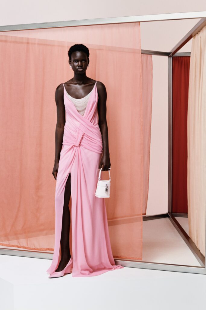 A fitted pink silk dress with a sleeveless design, V-neckline, and draped silhouette featuring a slit.