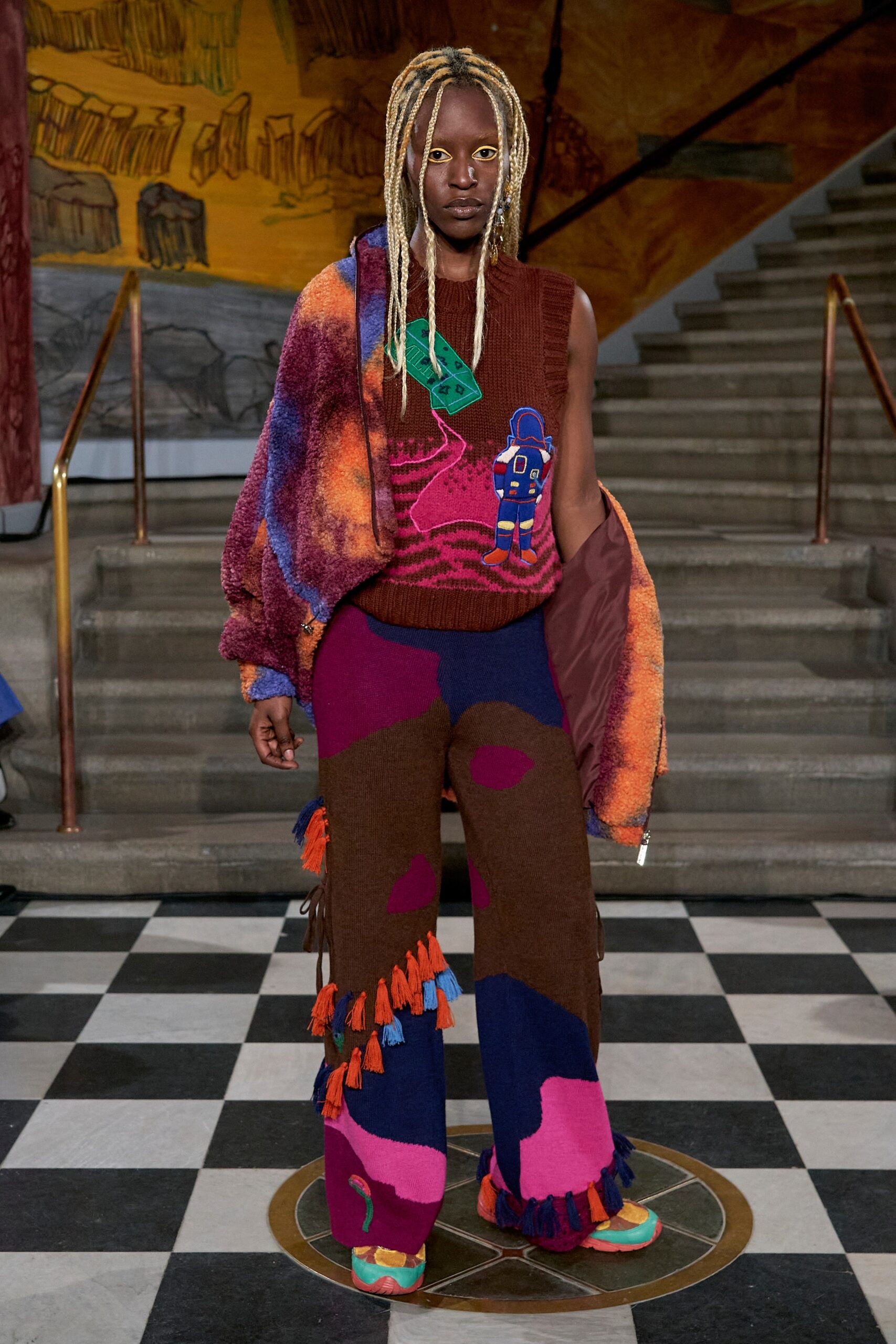 A relaxed multicolor sweater paired with fringed pants, showcasing a vibrant and artistic design.