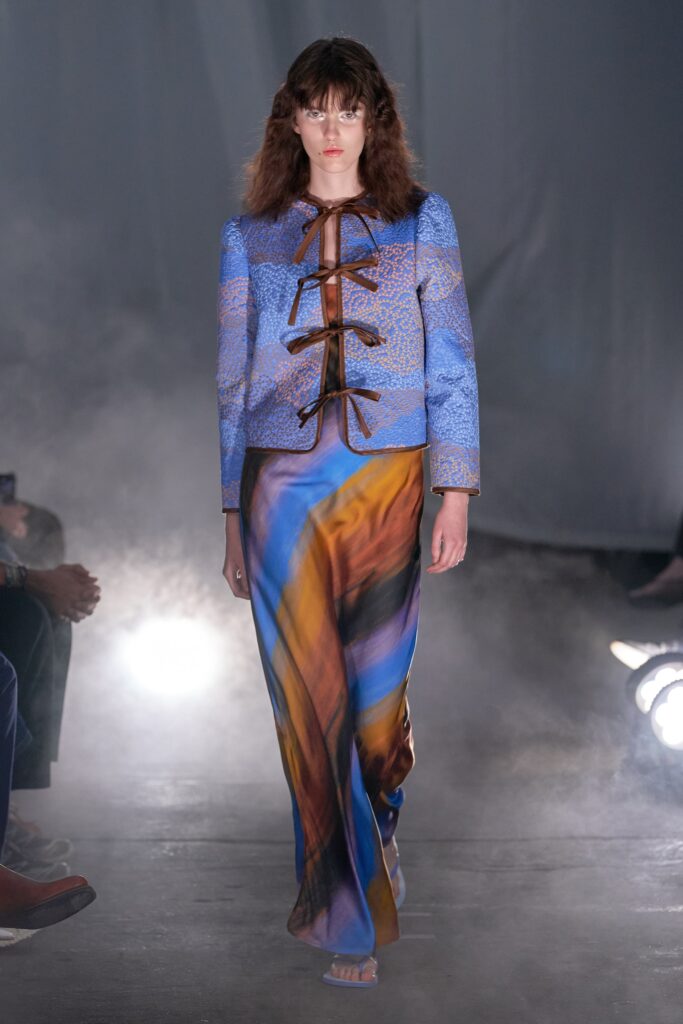 A fitted blue silk dress with long sleeves, a V-neckline, and an asymmetric design.