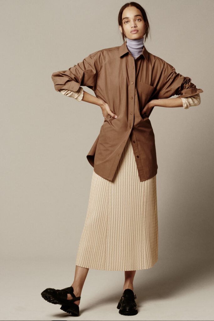 A relaxed brown cotton shirt with long sleeves paired with a pleated beige skirt.