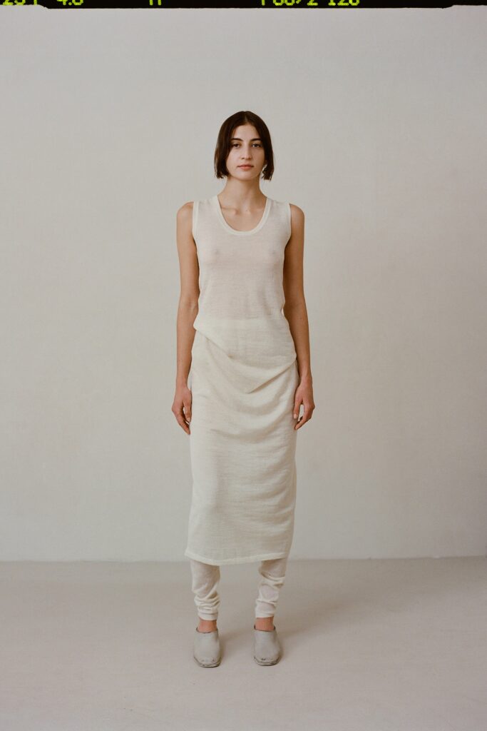 A fitted beige cotton sleeveless dress with a high neckline and draped design.