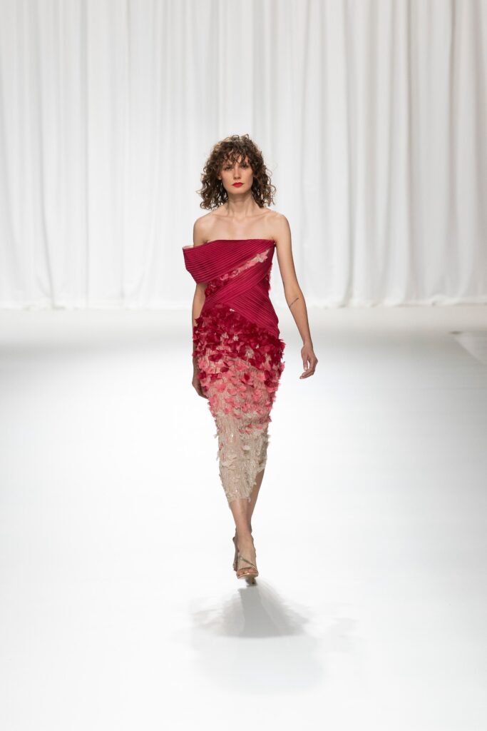 A fitted strapless dress featuring pleated detailing in red and beige with an asymmetric design.