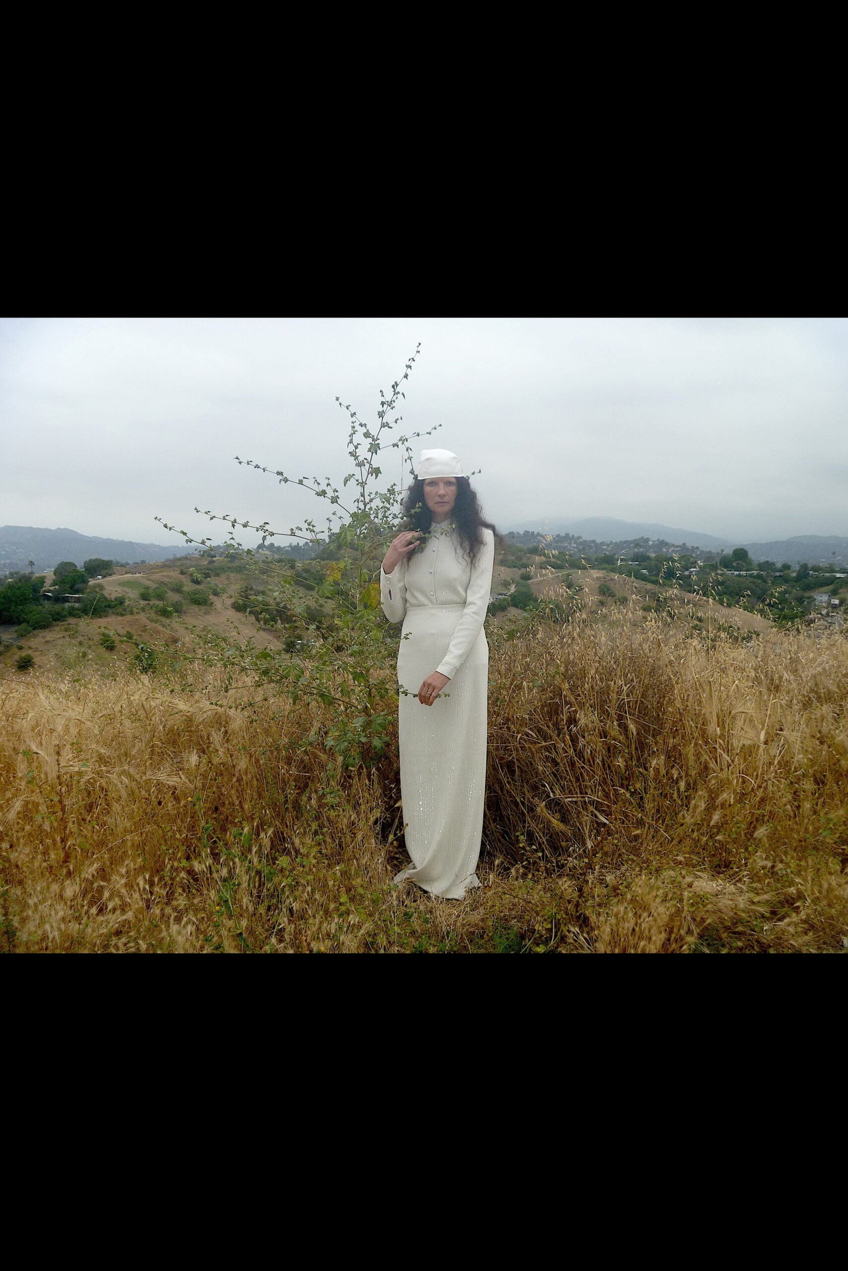 A fitted white silk dress with long sleeves, a high neckline, and a stylish slit.