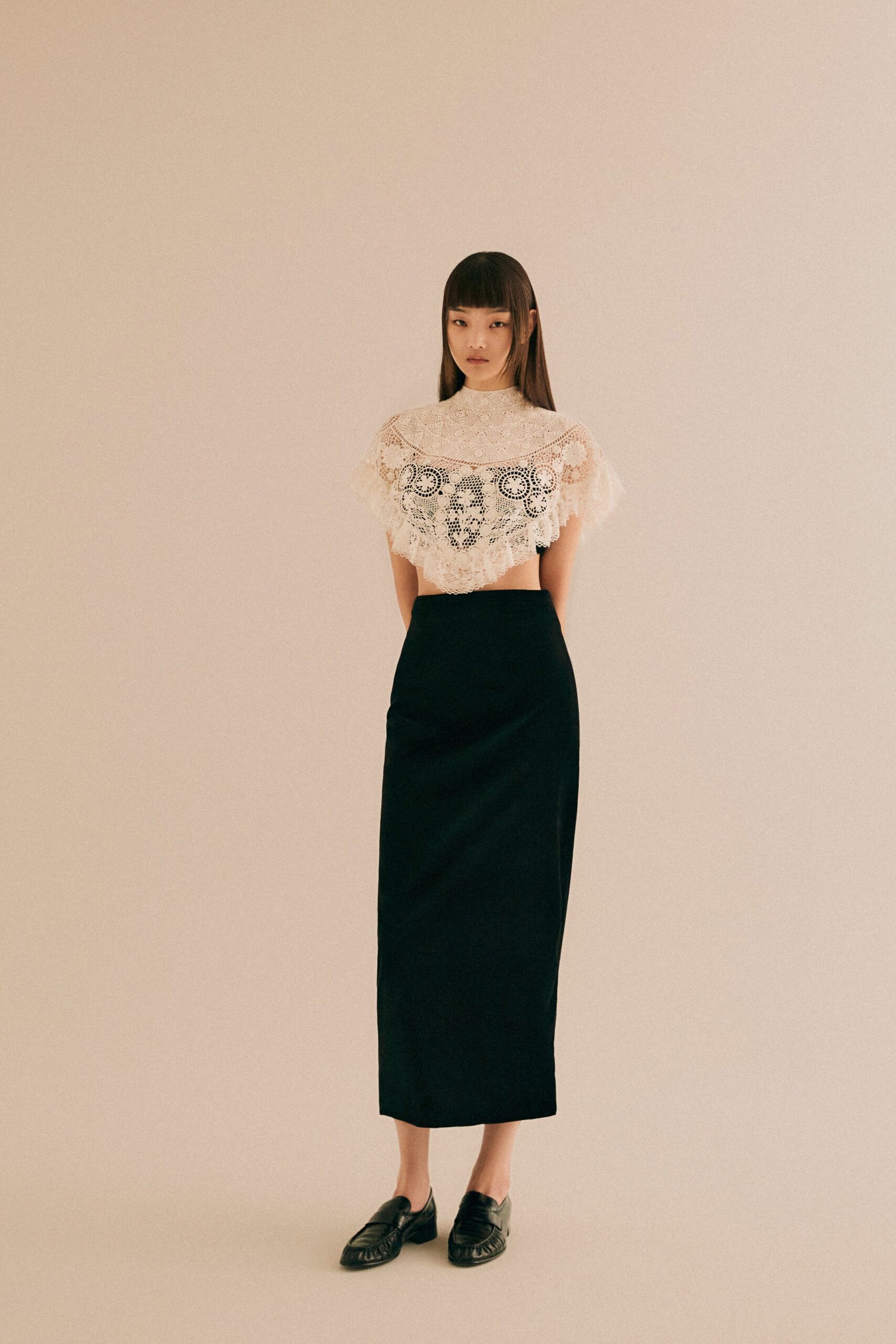 A fitted beige lace top with embroidery paired with a black fitted skirt.