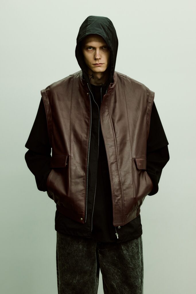 An oversized brown leather jacket with a hood, layered over a black shirt.