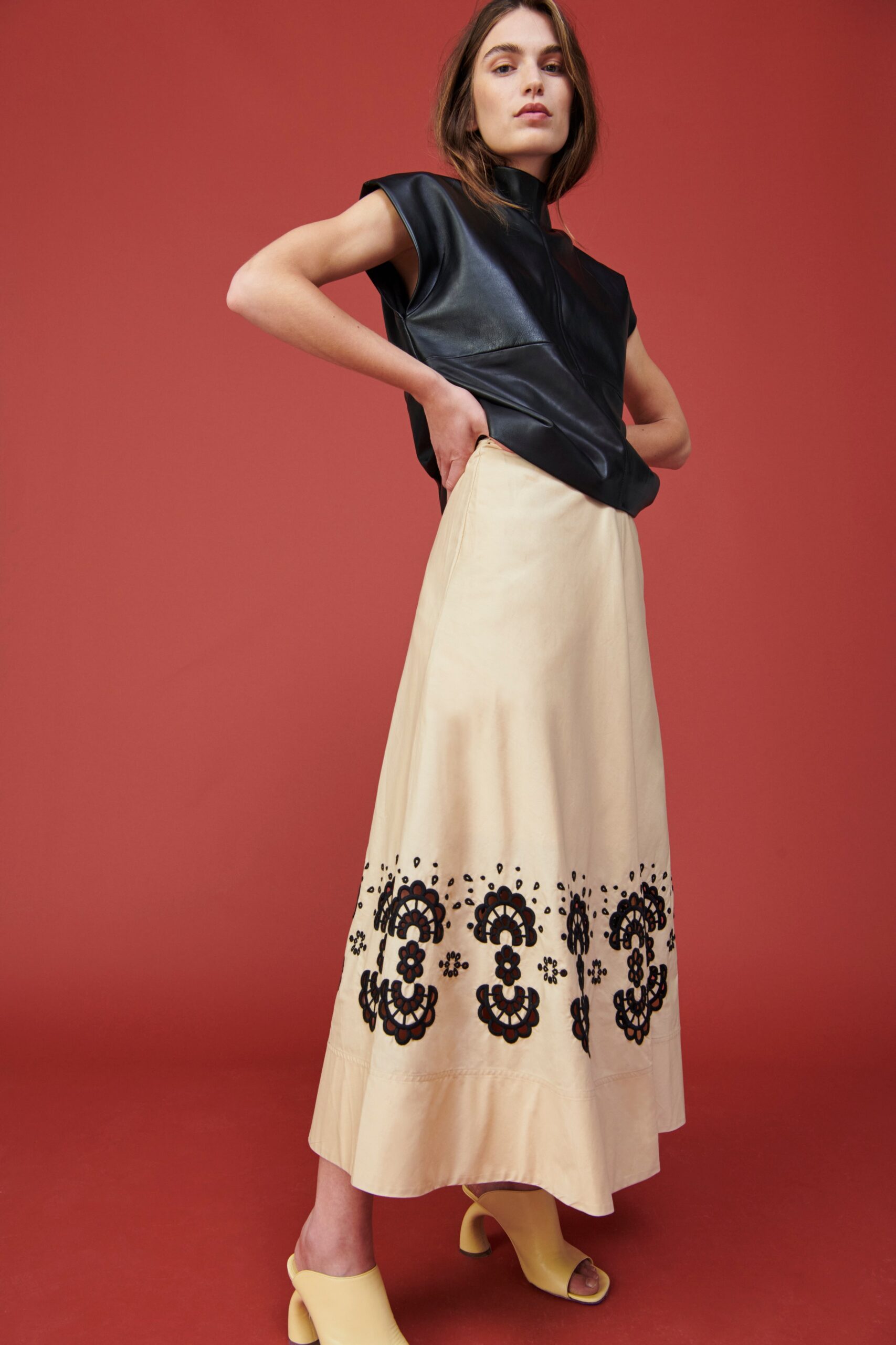 A fitted black leather sleeveless top paired with a beige maxi skirt featuring embroidered details.