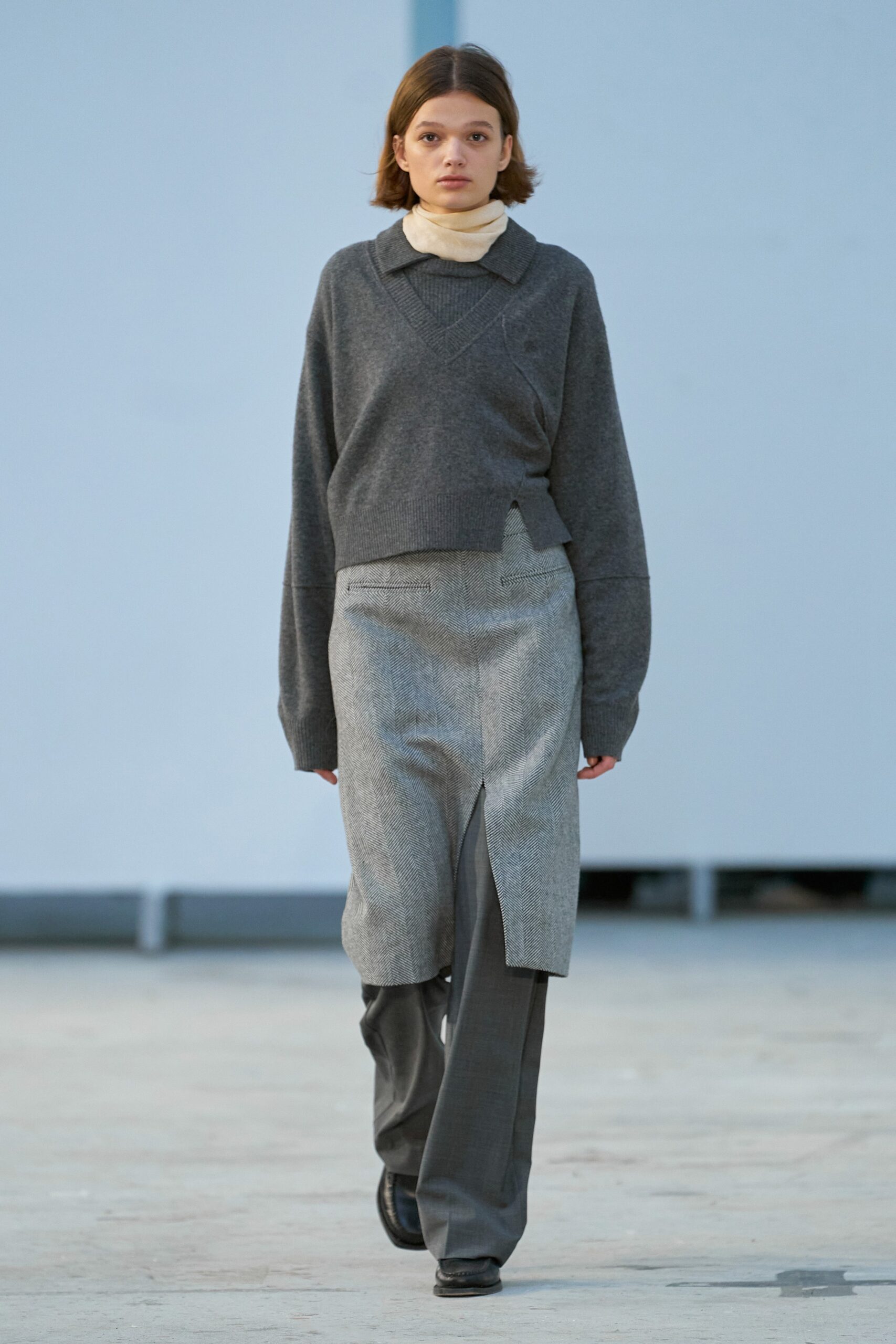 A relaxed gray sweater with long sleeves and a collared design paired with an asymmetric skirt.