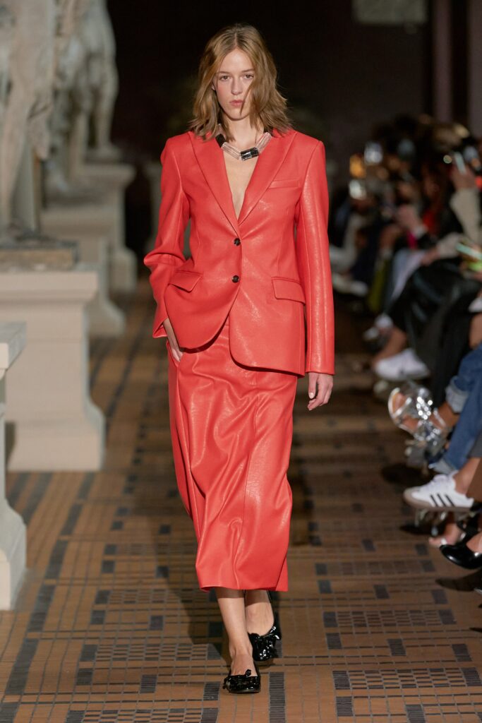 A fitted red leather suit featuring a V-neckline and asymmetric design details.