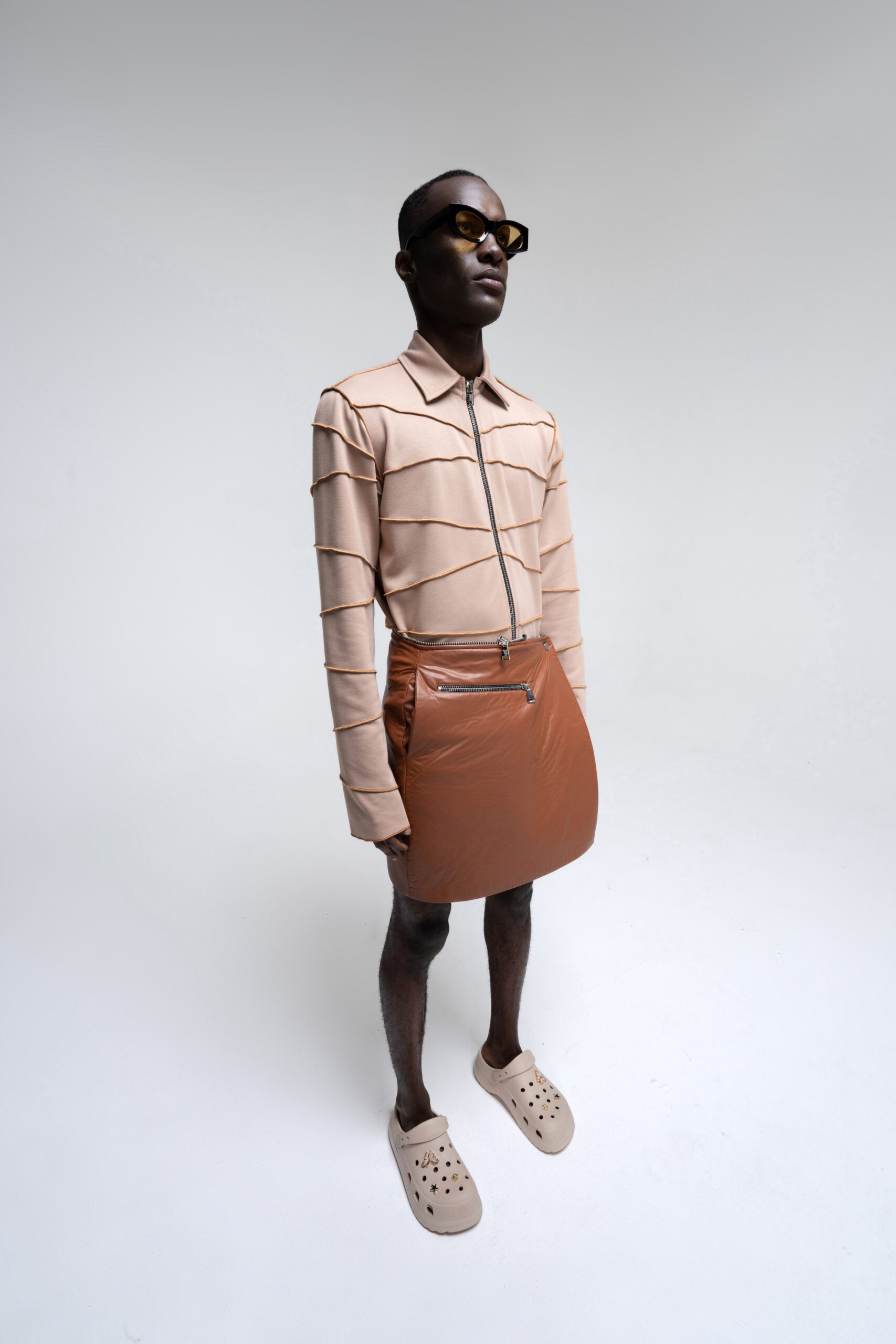 A fitted beige long-sleeve shirt with a collared neck and a brown zippered asymmetric skirt.