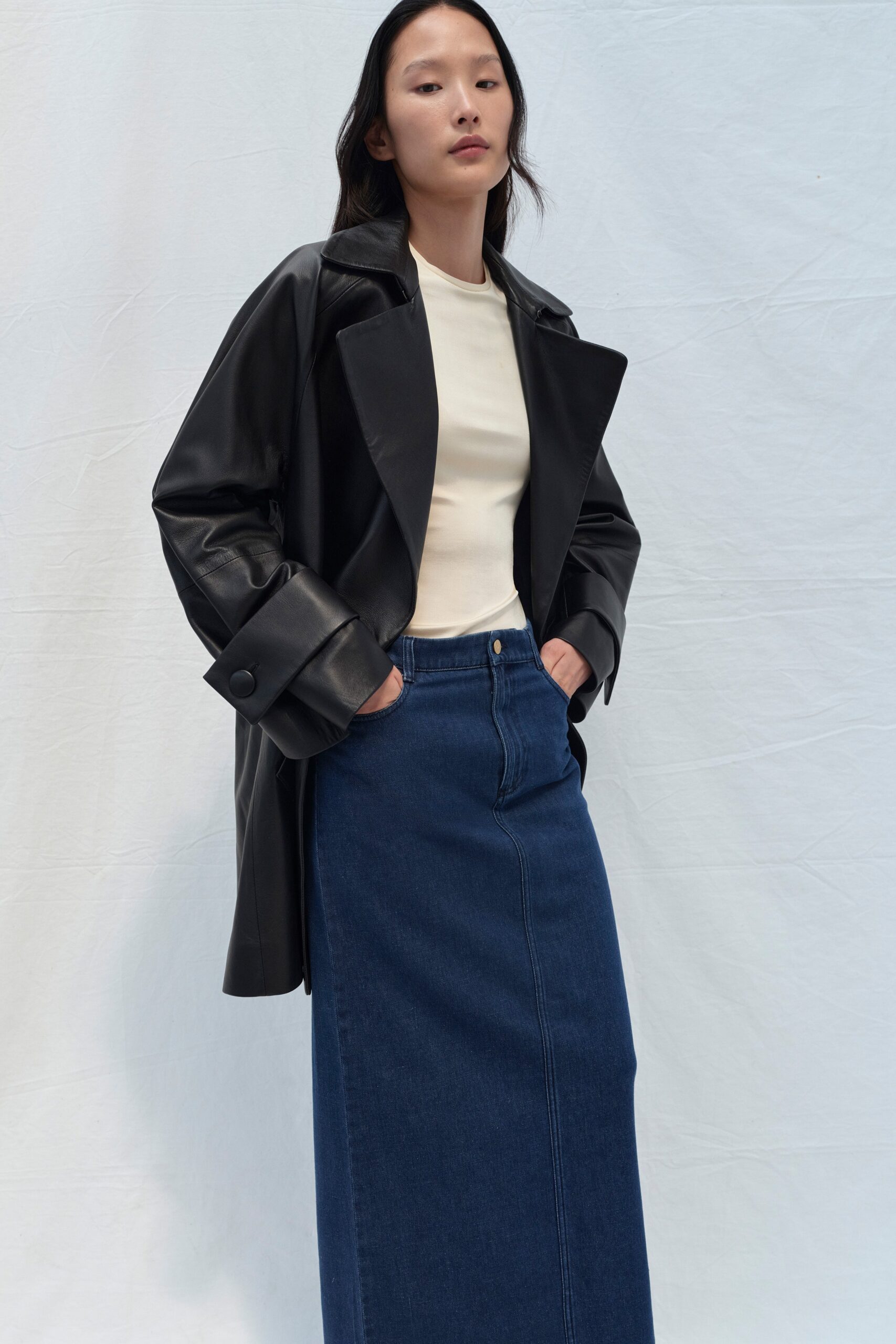 A fitted black leather coat paired with a straight-leg blue denim skirt.
