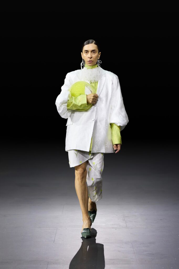 An oversized white jacket paired with green shorts, featuring a unique design and buttoned details.