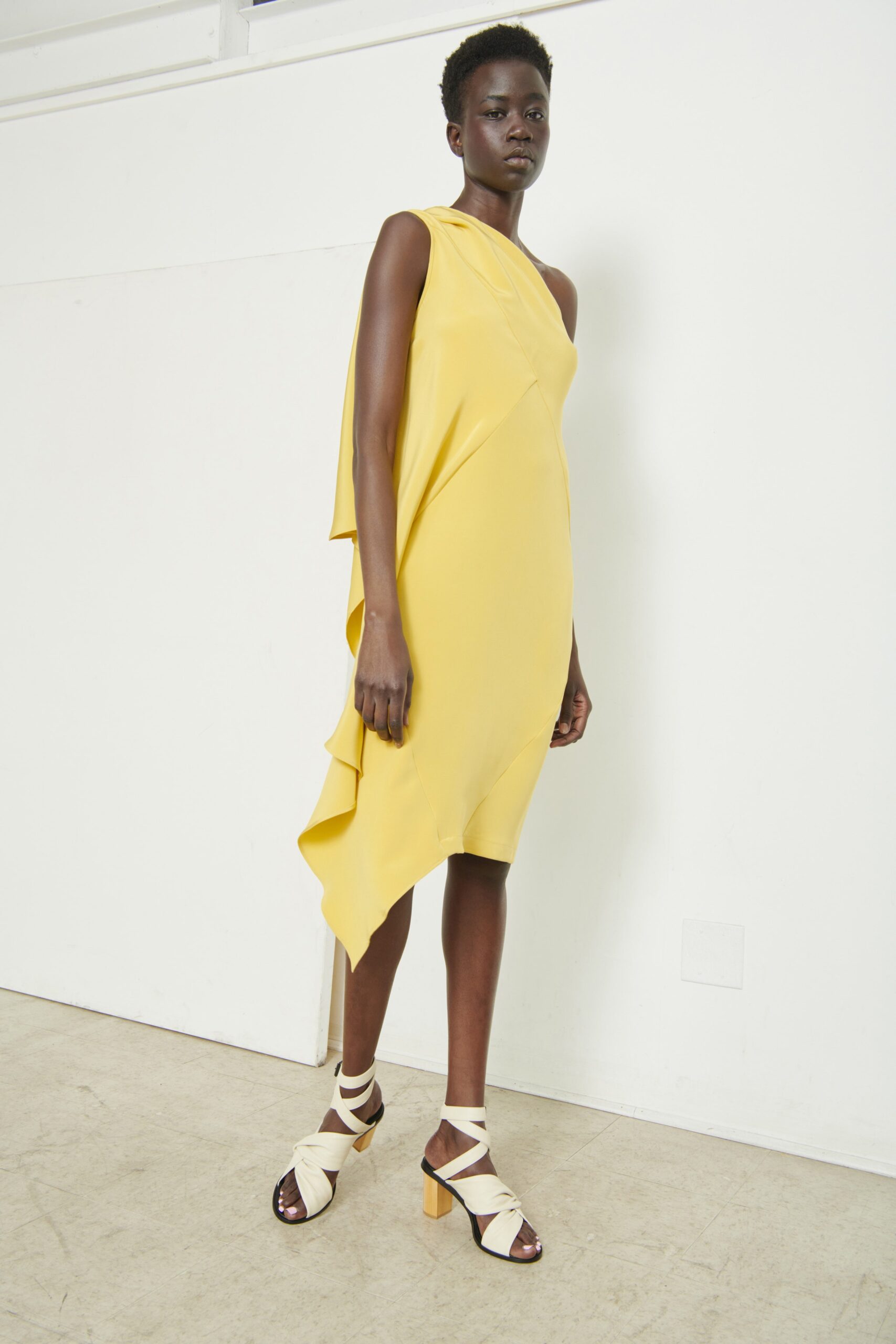A fitted yellow silk dress with an asymmetric design and draped detailing.