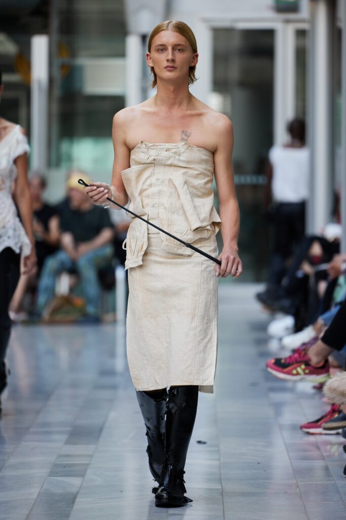 A fitted beige sleeveless dress with a unique design and knee-length hem.