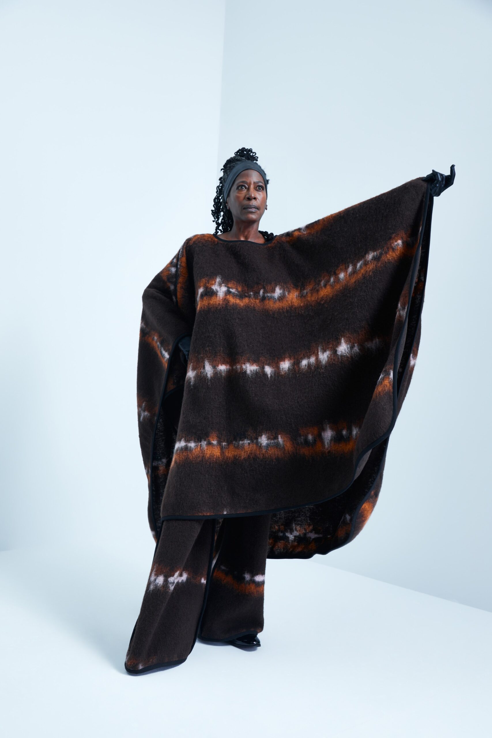 This ensemble features a relaxed poncho crafted from wool, showcasing a striking print that blends earthy tones of brown, orange, and white. The flowing silhouette creates a sense of movement, while the accompanying pants maintain a harmonious balance, enhancing the overall visual impact.