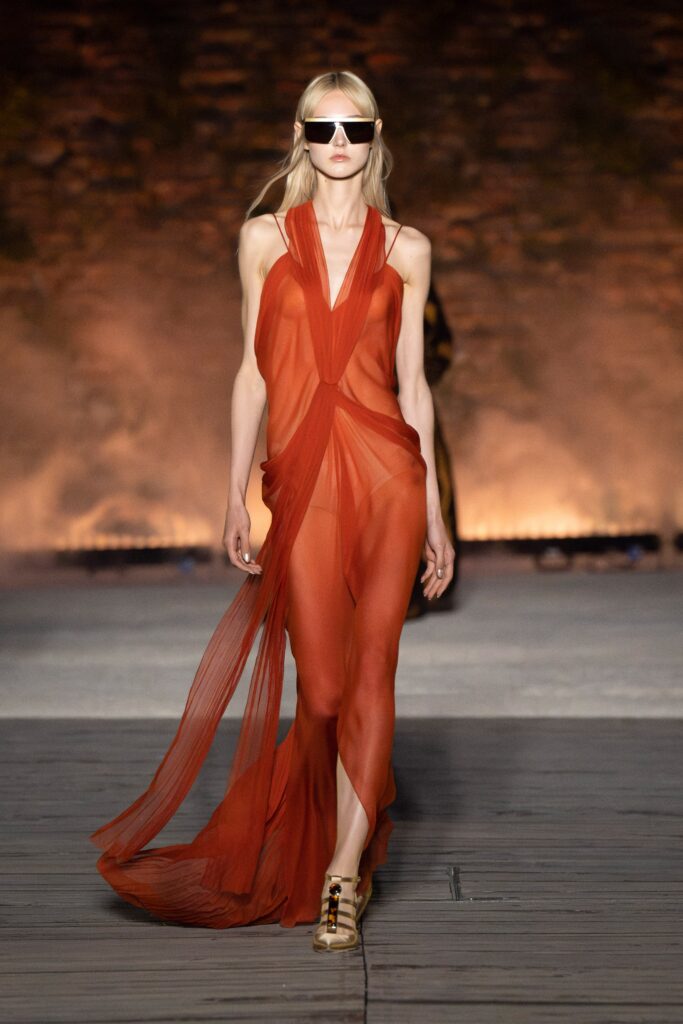 A fitted red silk sleeveless dress with a V-neckline and draped design.