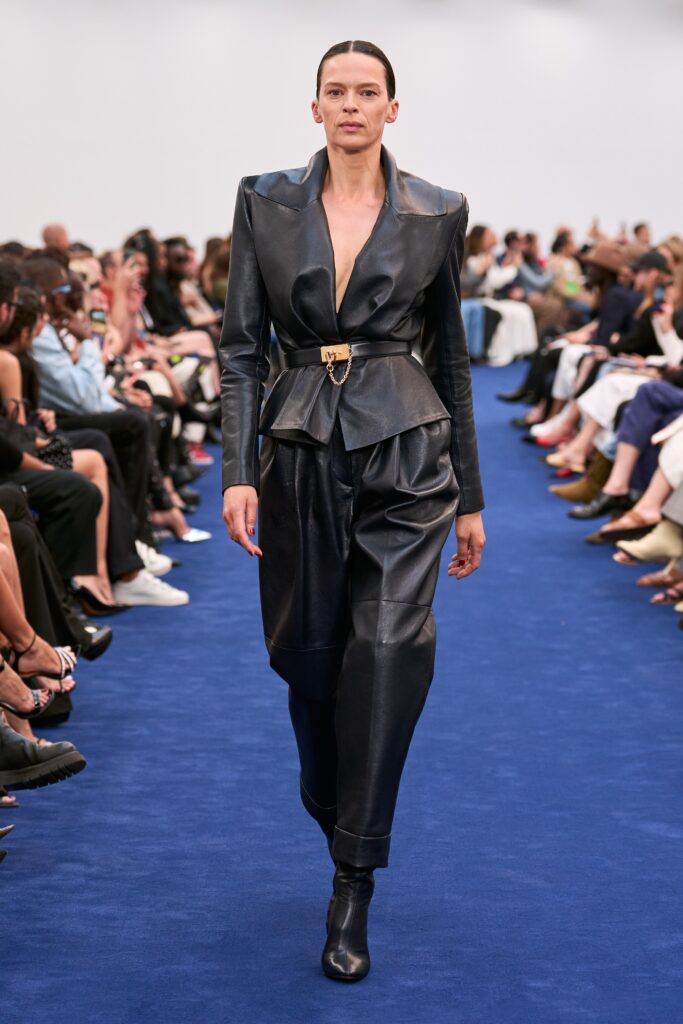 A fitted black leather jacket with a V-neck and structured pants, showcasing a modern silhouette.
