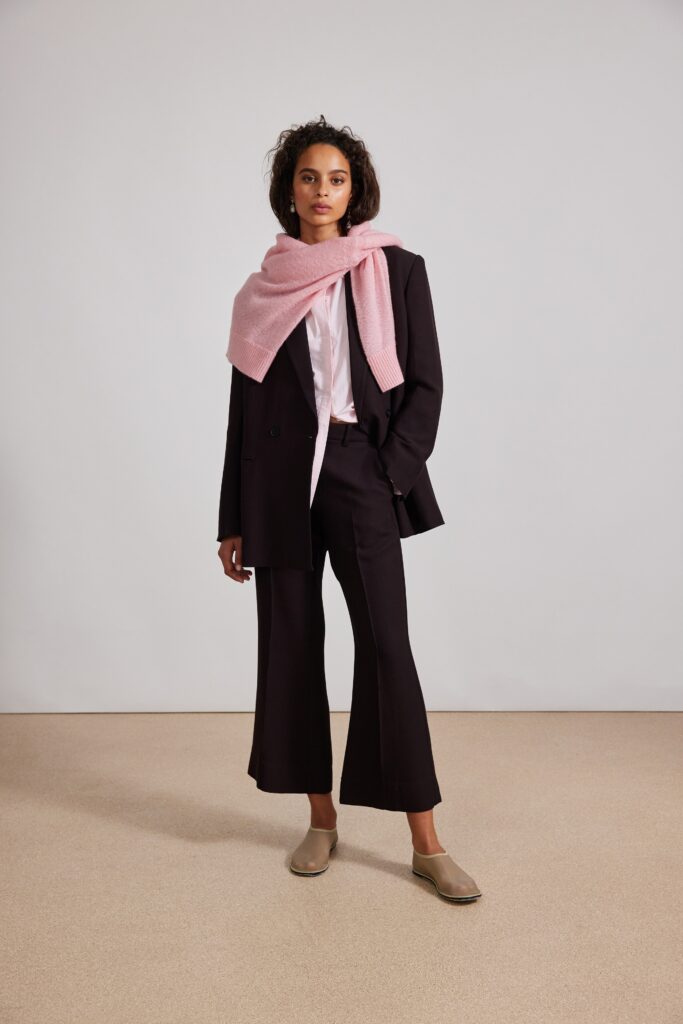 A tailored black suit with a collared shirt and flared trousers, complemented by a pink scarf.
