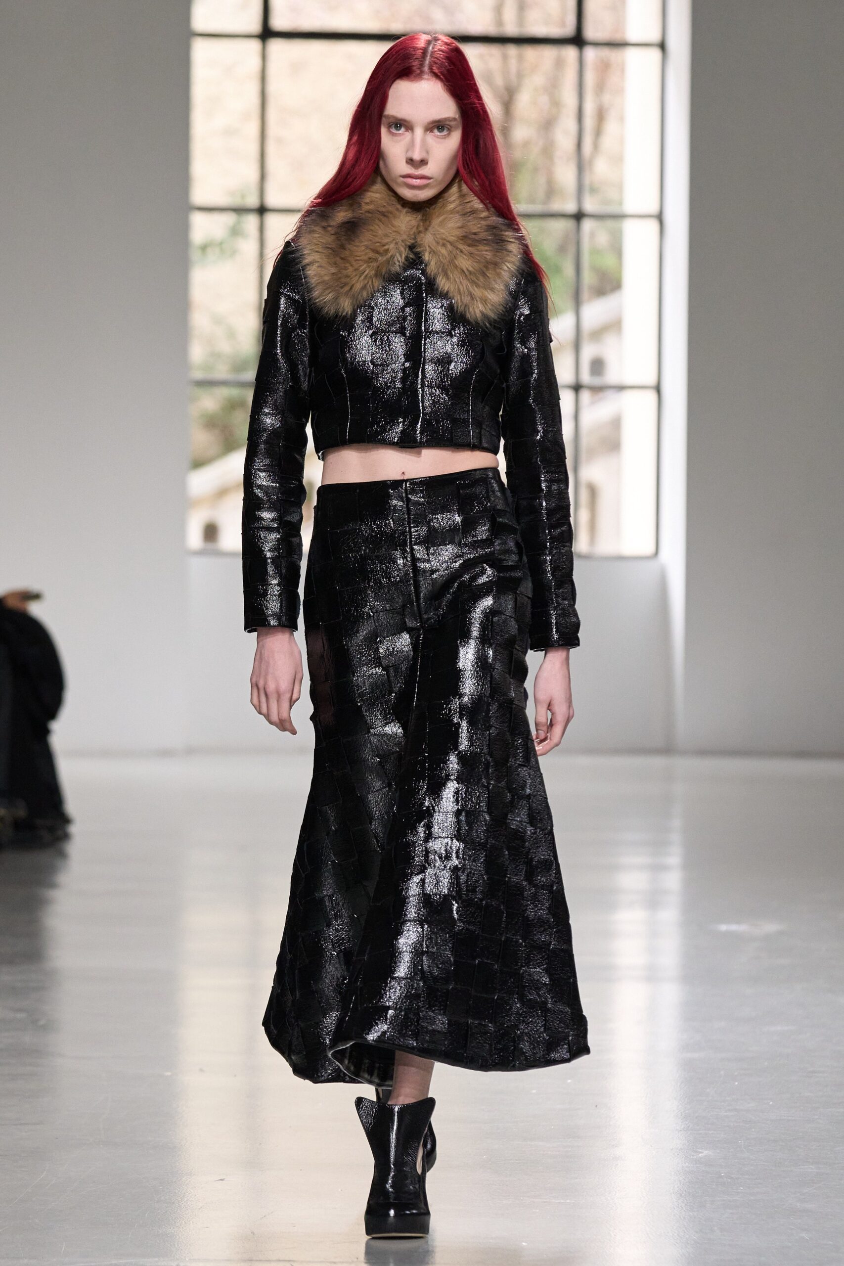 A fitted black leather jacket with a collar and a pleated asymmetric skirt.