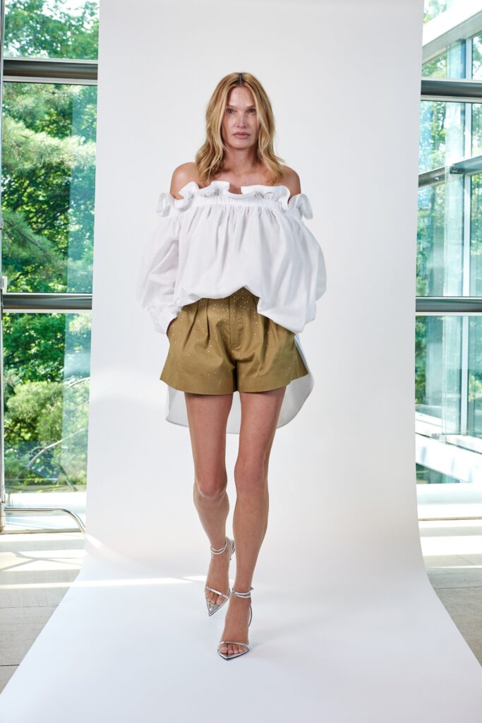 A relaxed white off-shoulder blouse with ruffles paired with pleated olive shorts.