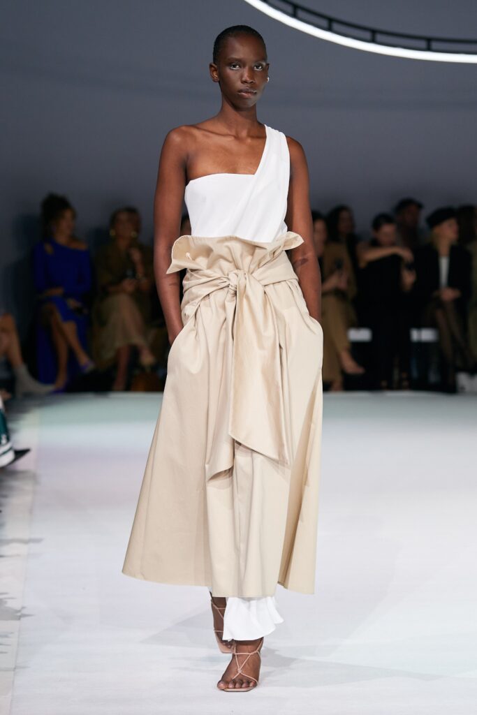 A fitted beige and white sleeveless dress with an asymmetric design and layered details.