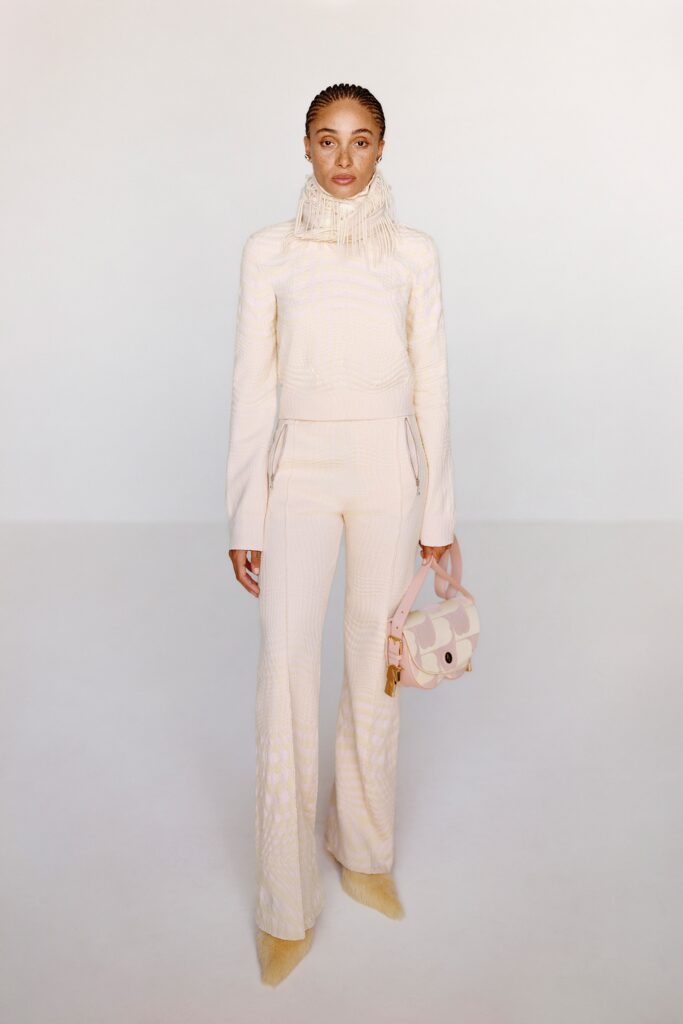 A fitted beige knit long-sleeve top with a high neck paired with flared pants.