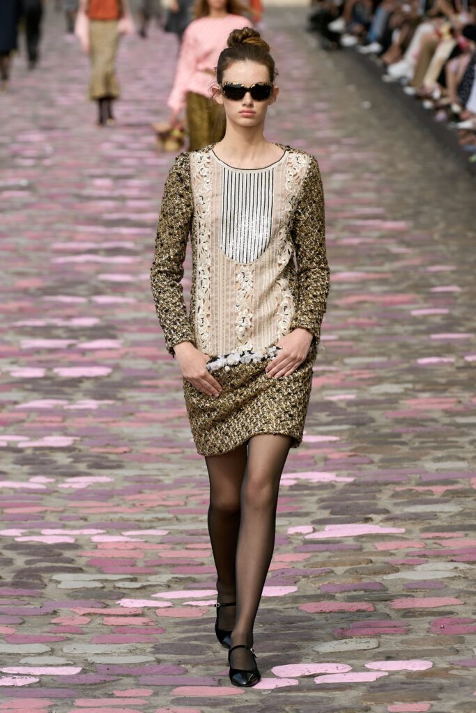 A fitted beige and gold long-sleeve dress with embroidered details and a layered design.