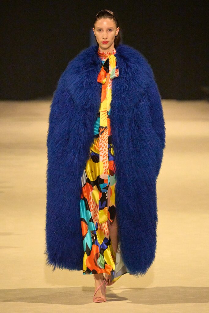 A fitted multicolor silk dress layered under a long-sleeve blue fur coat with a collared neckline.
